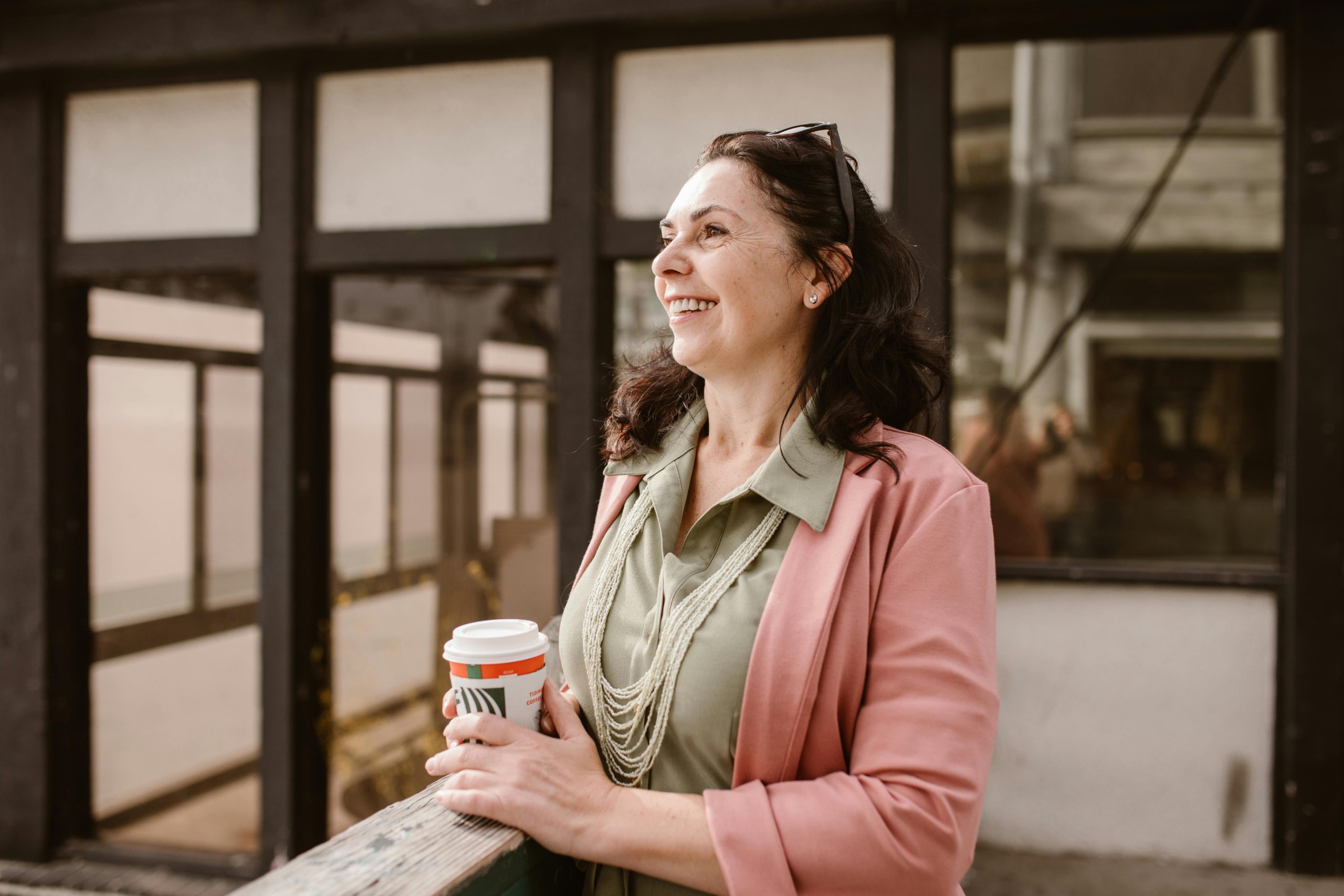 Brunette woman holding a take away coffee cup looking out over a balcony